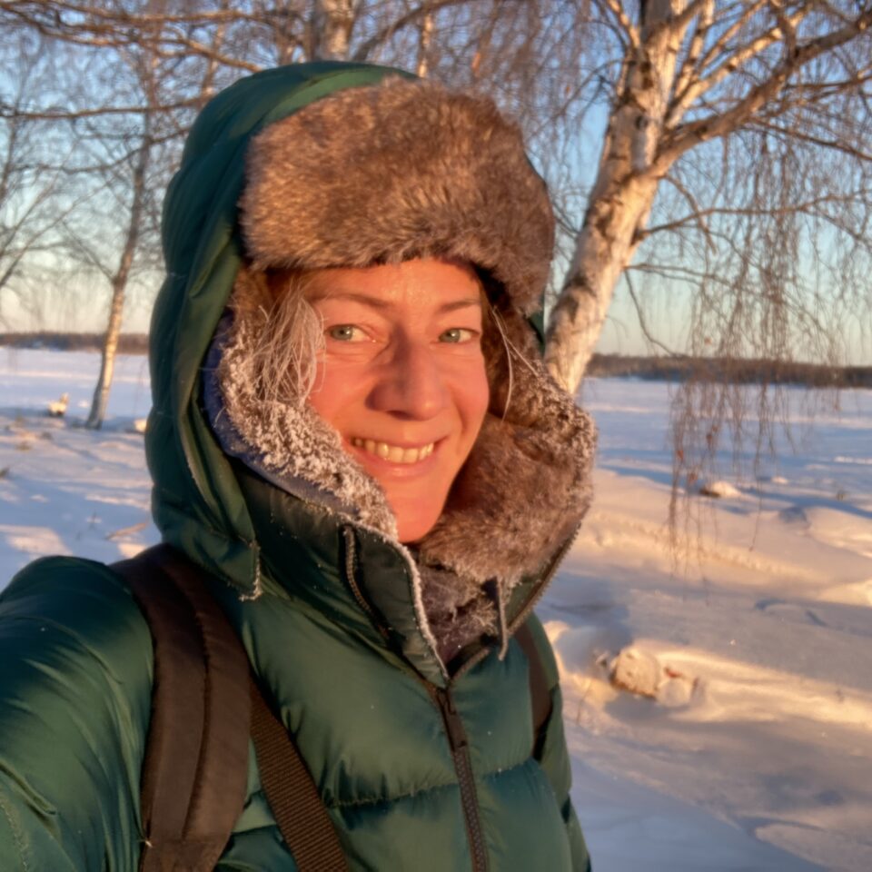 Bernadette Olderdissen i en grön vinterjacka med huvan uppdragen och ett soligt vinterlandskap i bakgrunden.
