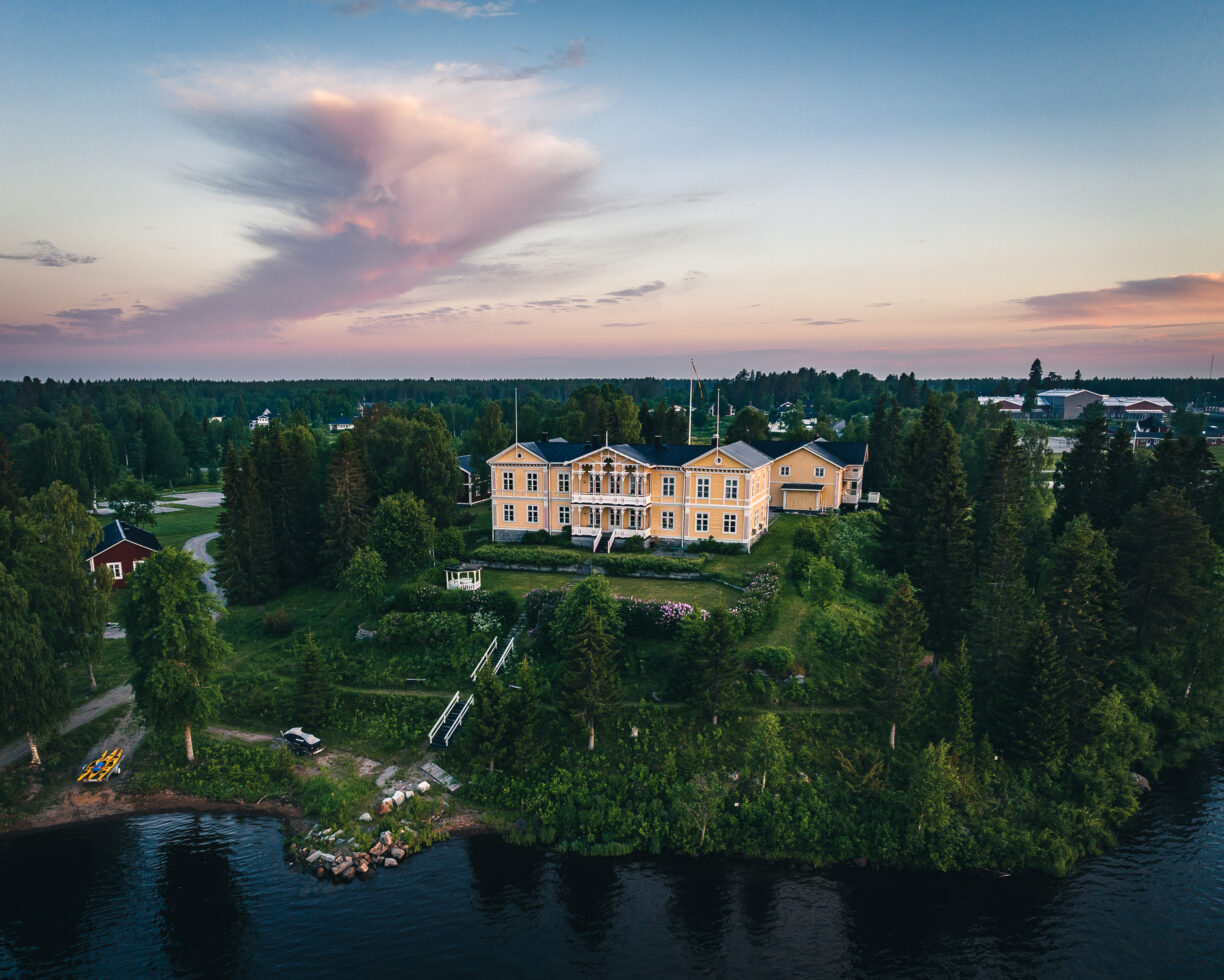 Vybild över Filipsborg herrgård där Kalixälven syns i nedre delen av bilden. Gröna ytor med gräs och träd omfamnar den gula herrgården.