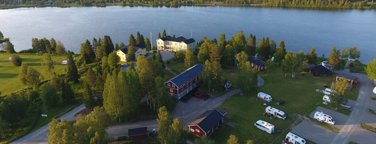 Vybild över en gul herrgård vid Kalixälven och en campingplats till höger om herrgården.