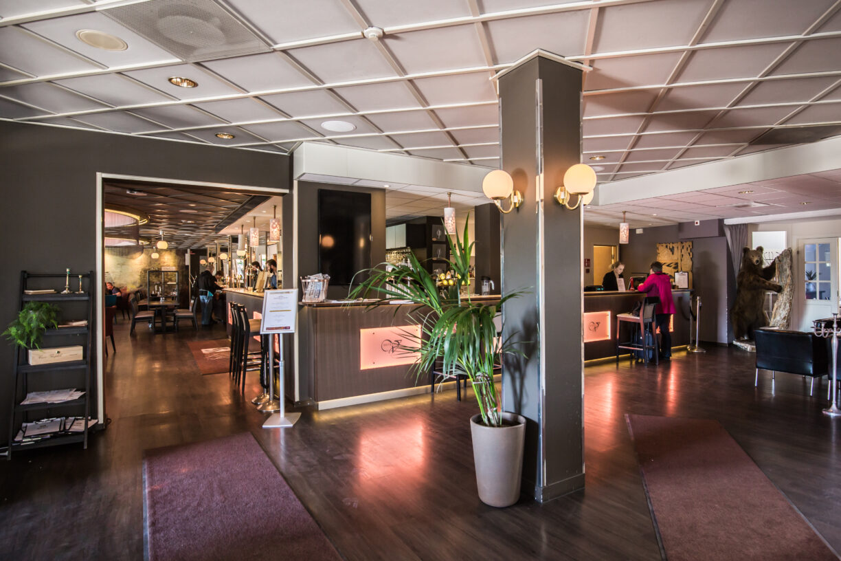 Hotell Valhalls reception där man ser in i restaurangen samt 2 personer som står vid receptionsdisken. Det står även en uppstoppad björn till höger i bilden.