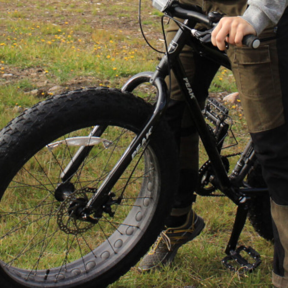 En fatbike som hålls av en människa stående på grästäckt mark.