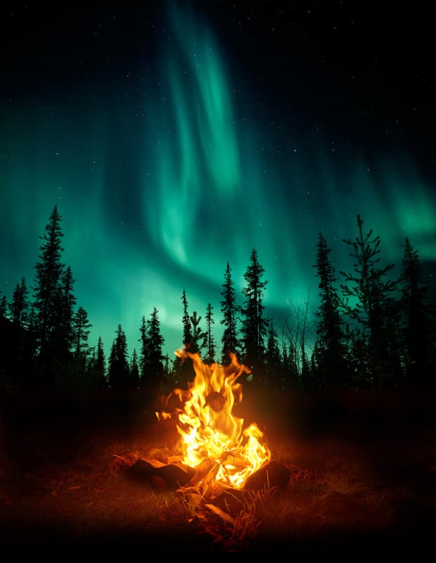 En brasa i skogen med norrsken i bakgrunden.