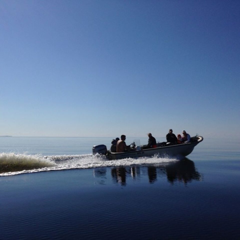 En motorbåt med flertalet människor åker på ett spegelblankt vatten med blå himmel.