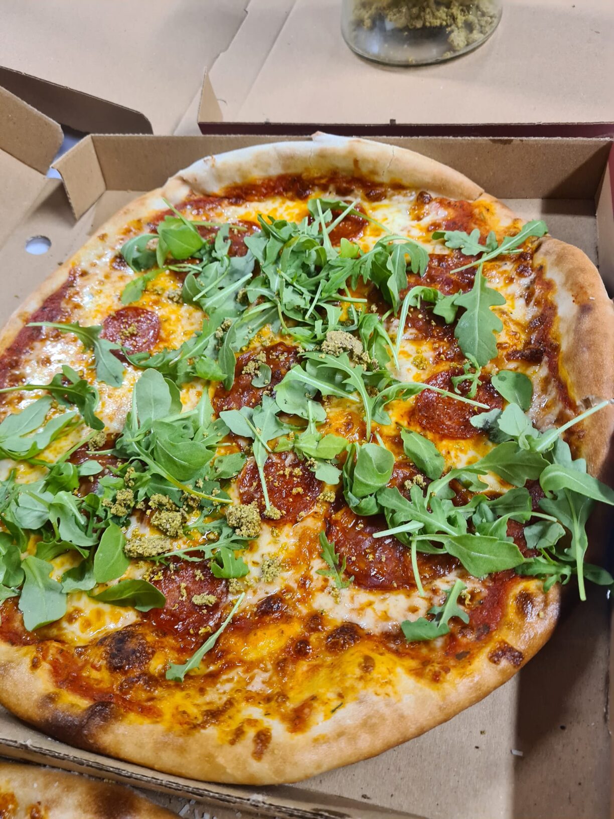 En färdiggräddad pizza i kartong fylld med tomatsås, ost, salami och ruccola på toppen.