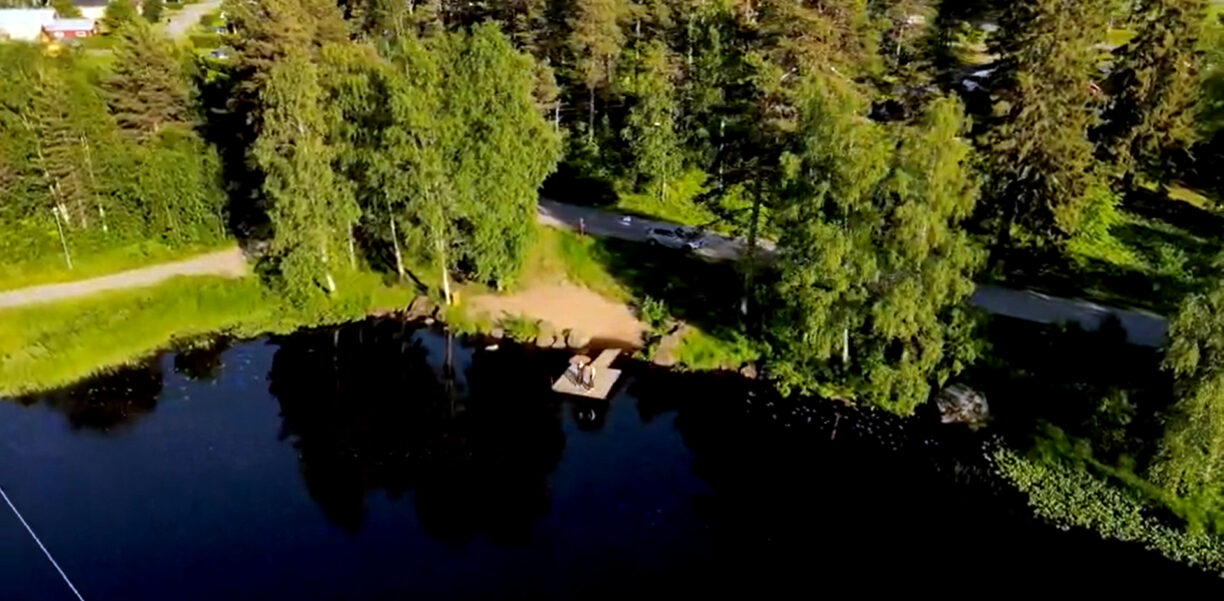 En brygga vid en liten strand och mörkblått vatten, en solig sommardag.