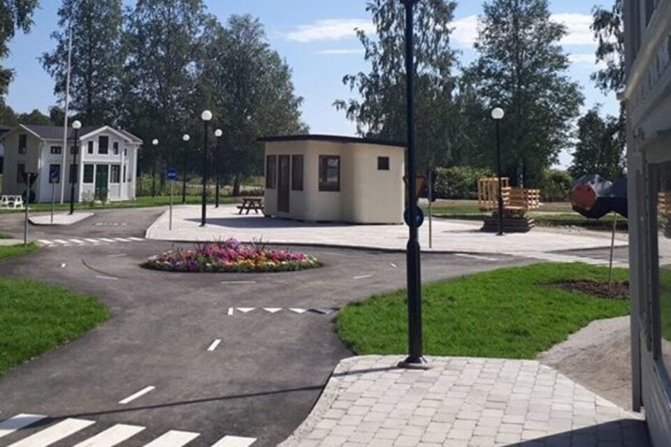 En miniatyr-stad med asfalterad väg, små trähus, lyktstolpar och träd.